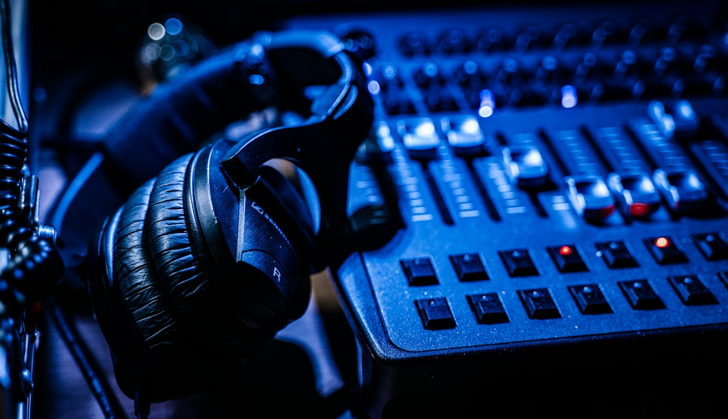 Black headphones on an audio mixing console with blue light.